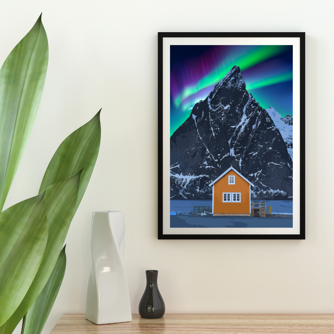 Framed poster from the mountain Olstind in Lofoten, Norway. Yellow house below the mountain and northern light is dancing in the sky. White wall and flower and decorations around.