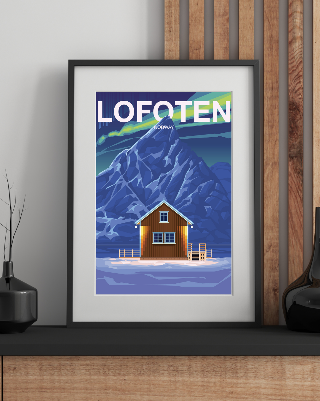 Framed poster of Lofoten with Olstind mountain and the classic yellow cabin in the front, design on a wall. Colors are blue and green, and the northern lights are dancing in the sky.