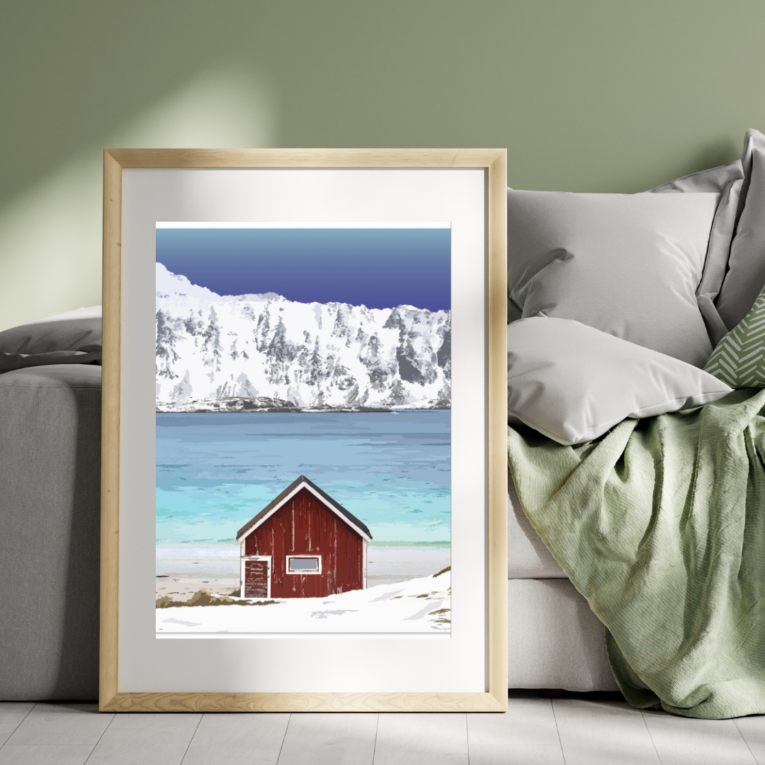 Framed print of a the classic red cabin at the Ramberg beach in Lofoten, Norway with snowcapped mountains, displayed in a bed room.