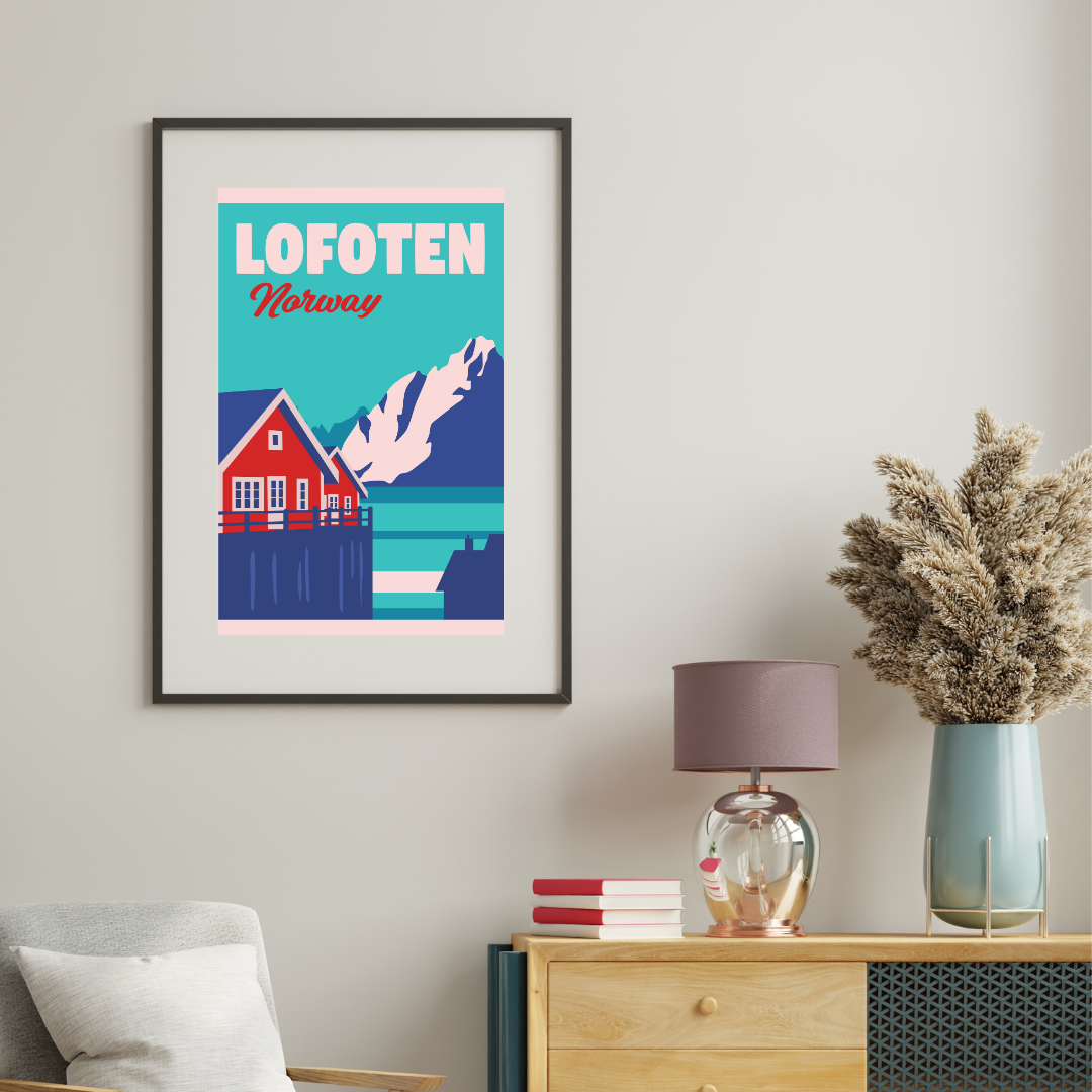 Framed poster of Lofoten, Norway with a rorbu (fishermans hut) and mountain on a wall above a wooden dresser.