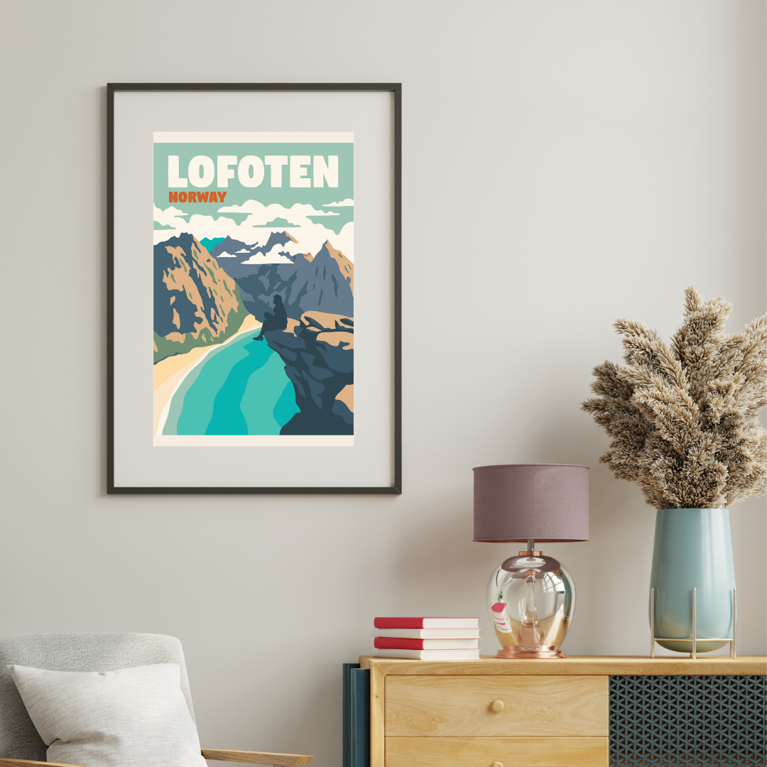 Framed poster from Ryten in Lofoten, Norway on a wall above a wooden dresser with decorative items. On the picture a person is sitting on the classic Ryten cliff and looking down over Kvalvika beach and the ocean.