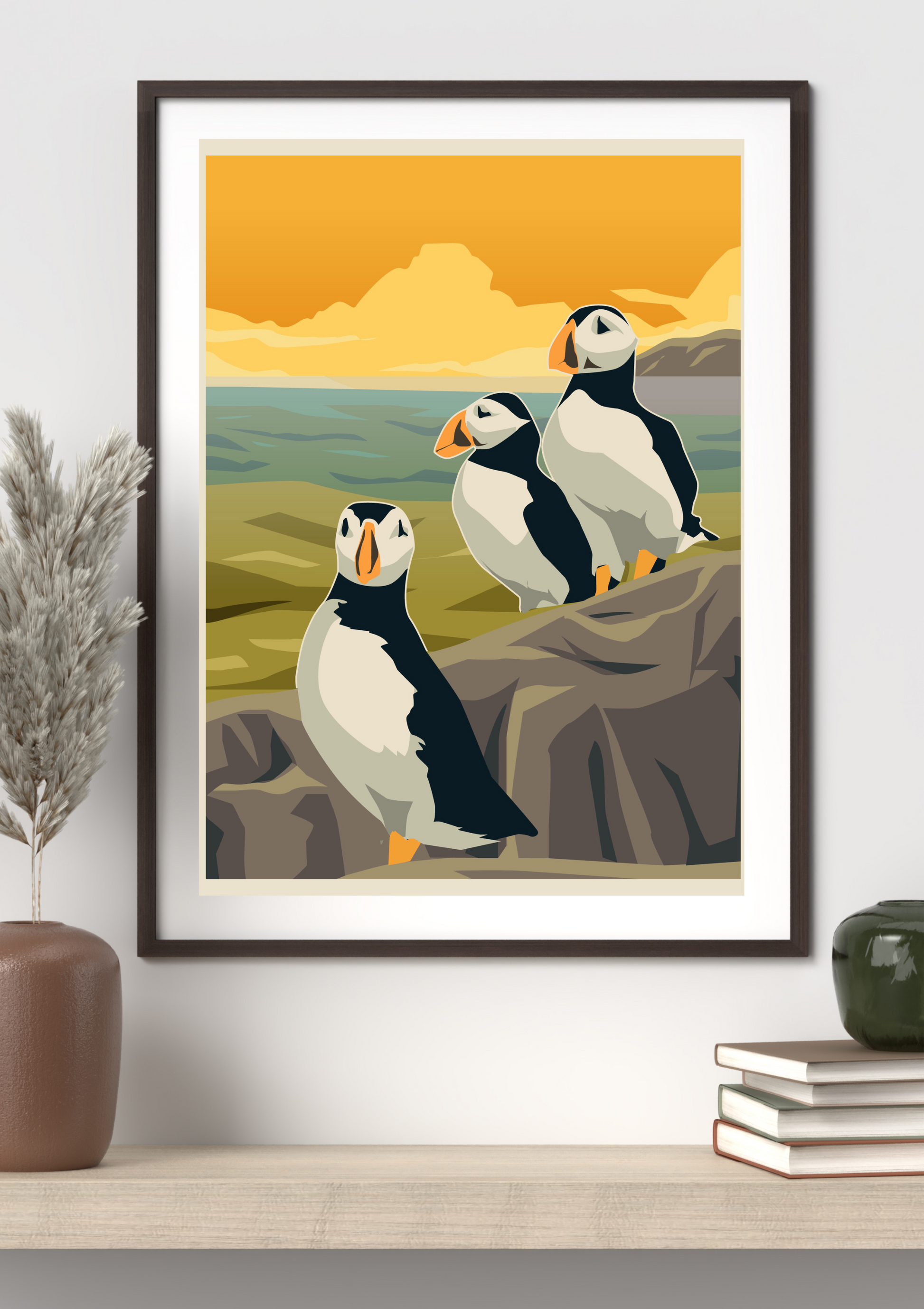 Framed artwork of puffins on a rock with a scenic background, displayed on a wall.